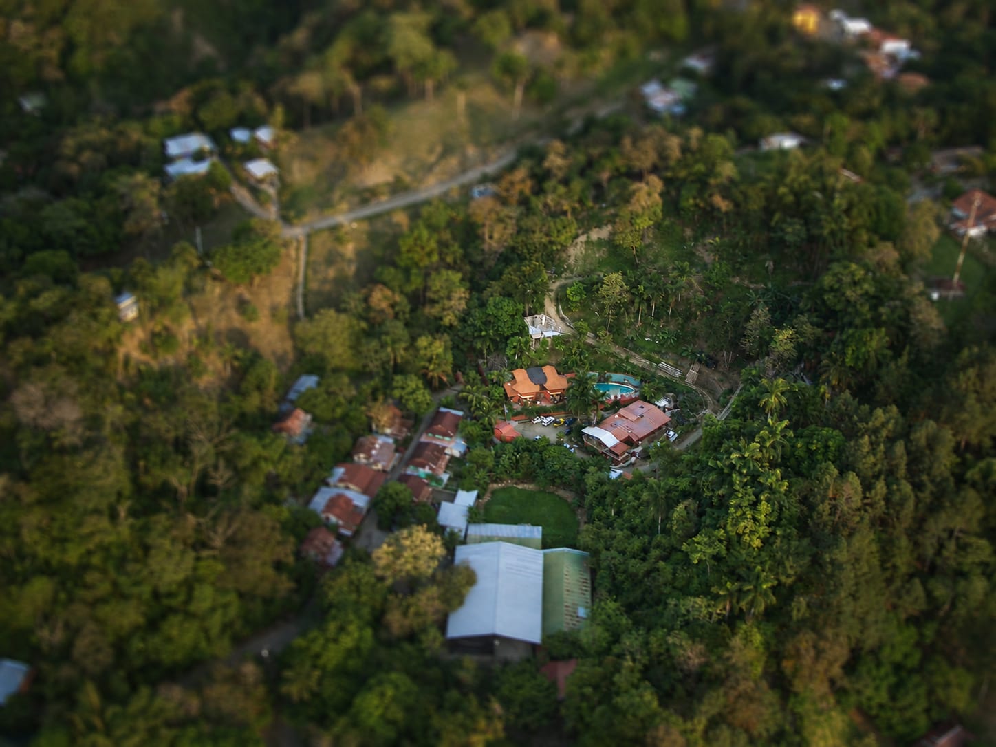 Fotografía aérea del hotel y las casas vecinas sobre una loma boscosa arriba de Quepos, techos rojos y verdes entre los árboles y un camino que pasa junto a ellos