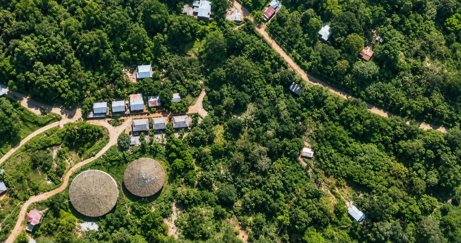 Vista aérea de la propiedad selvática sobre Quepos, con caminos de tierra entre construcciones dispersas y dos techos redondos de palma entre los árboles