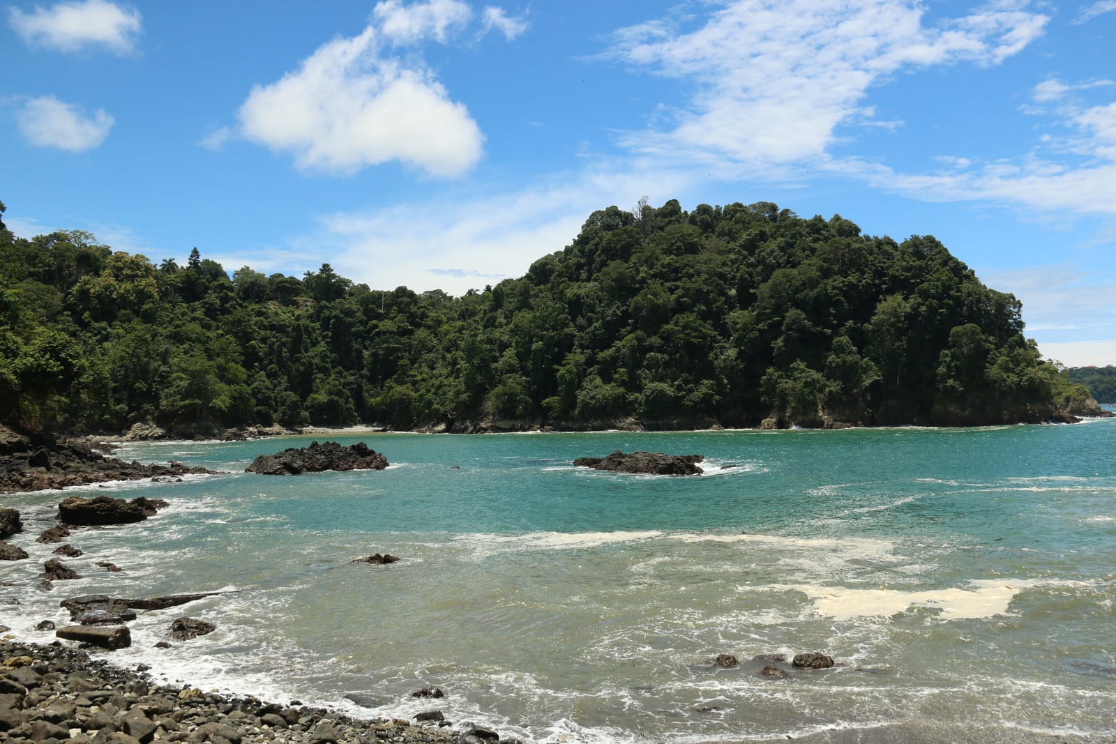A cove on the Manuel Antonio coast, rocks in the foreground and forest on the headland