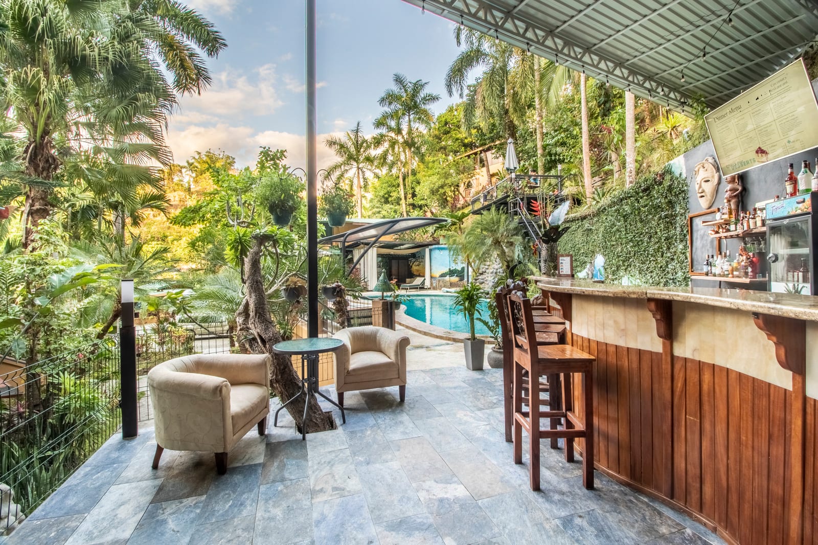 Armchairs and a small table beside the bar at golden hour, with the pool and palms directly behind