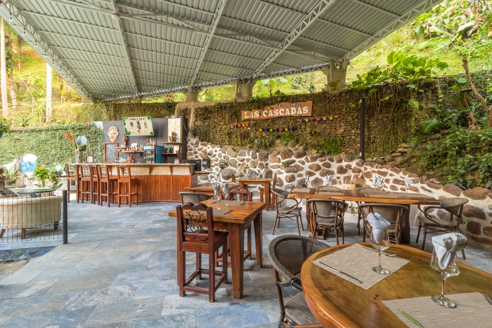 The terrace in daylight, with the wooden bar and its stools at one end and a living wall of plants carrying the Las Cascadas sign