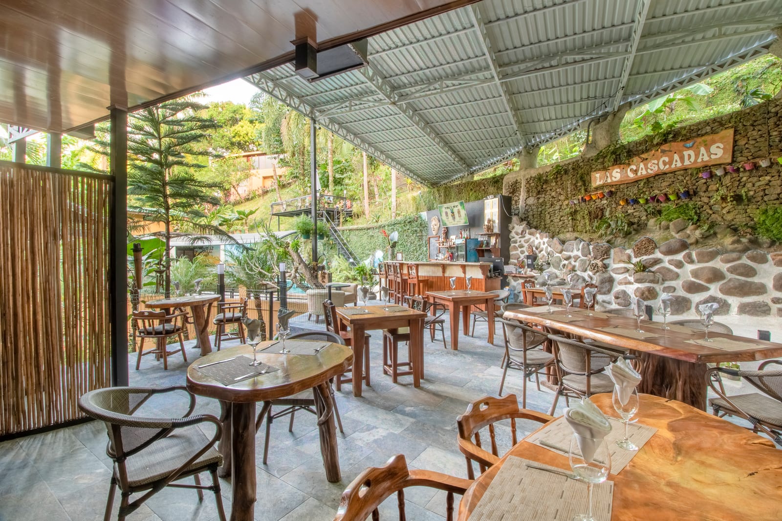 The terrace open along its length to the jungle, tables and rattan chairs under the roof, a tall pine and green hillside outside