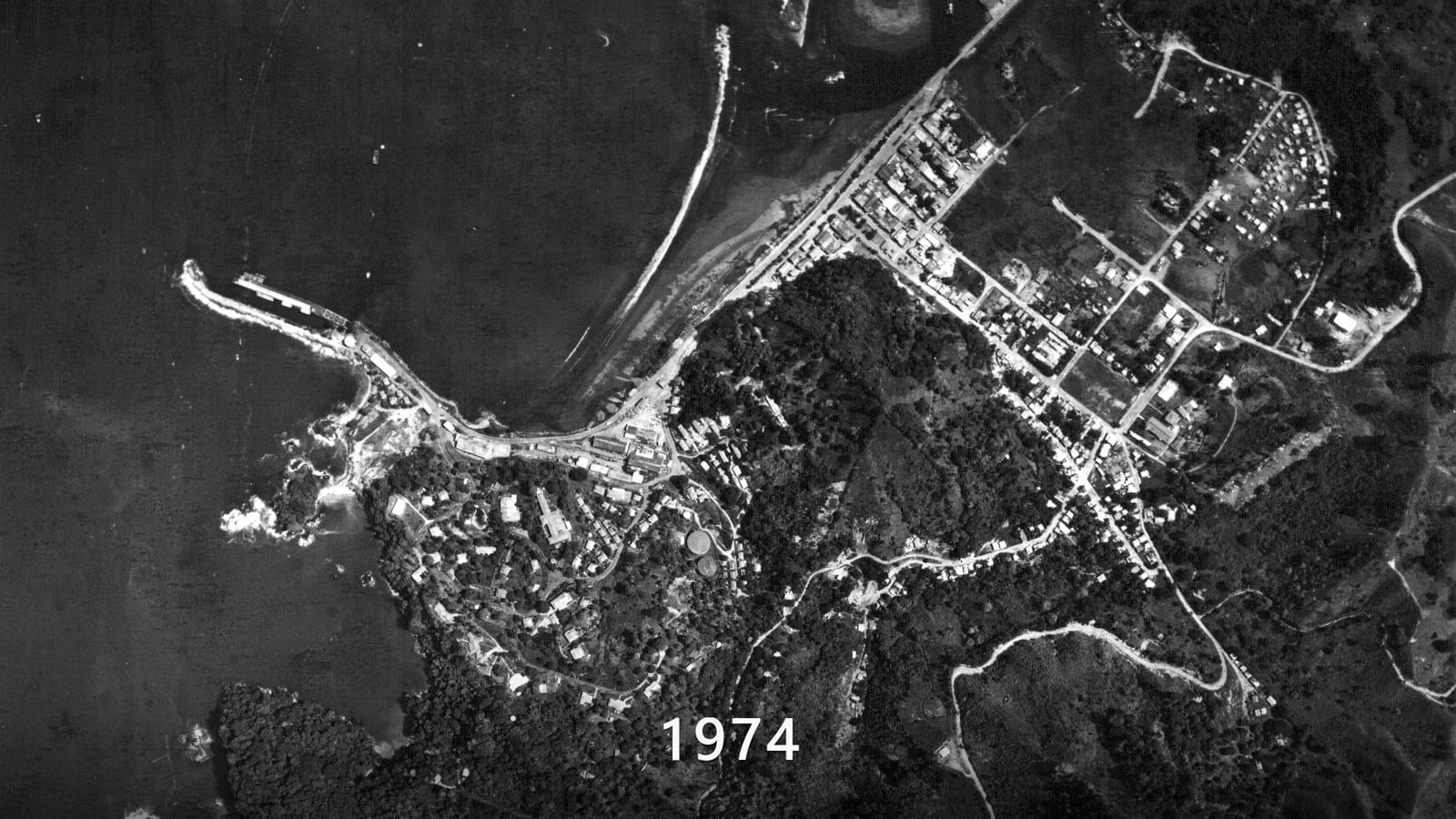 The first of the five surveys, flown in 1974: Quepos from directly above in black and white, the town on its headland, the sand spit closing the estuary and a pier reaching into the bay